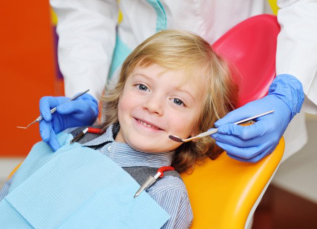 Menino sentado numa cadeira de dentista sorrindo e sendo examinado