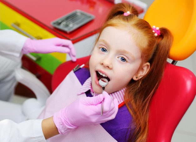 Menina sentada numa cadeira de dentista sendo examinada e com a boca aberta