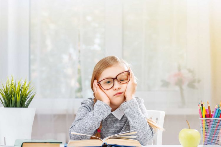 Uma estudante cansada está sentado em uma mesa com uma pilha de livros - Artigo Orthoclin