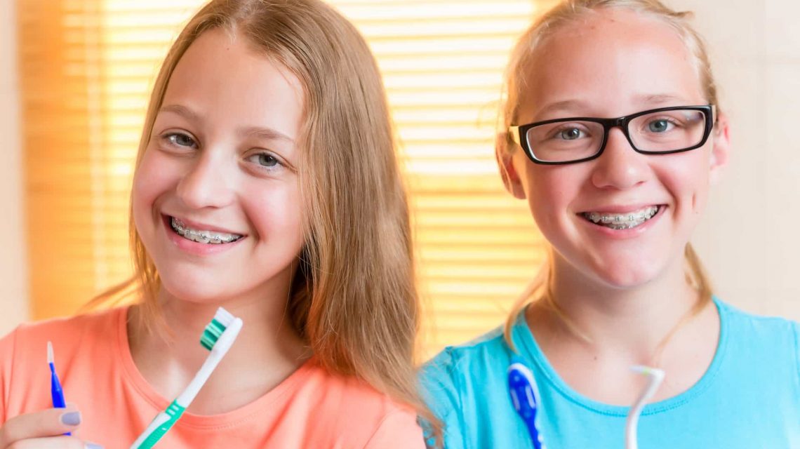 2 meninas sorrindo segurando escovas de dentes