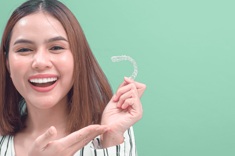 Mulher sorrindo enquanto segura um alinhador transparente, representando dicas de tratamento ortodôntico eficazes.