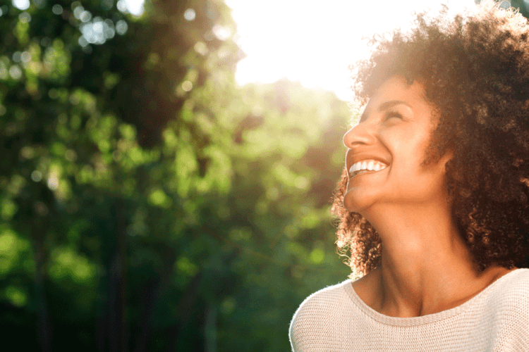 Mulher sorrindo ao ar livre após passar por tratamento ortodôntico estética, mostrando um sorriso saudável e perfeito.