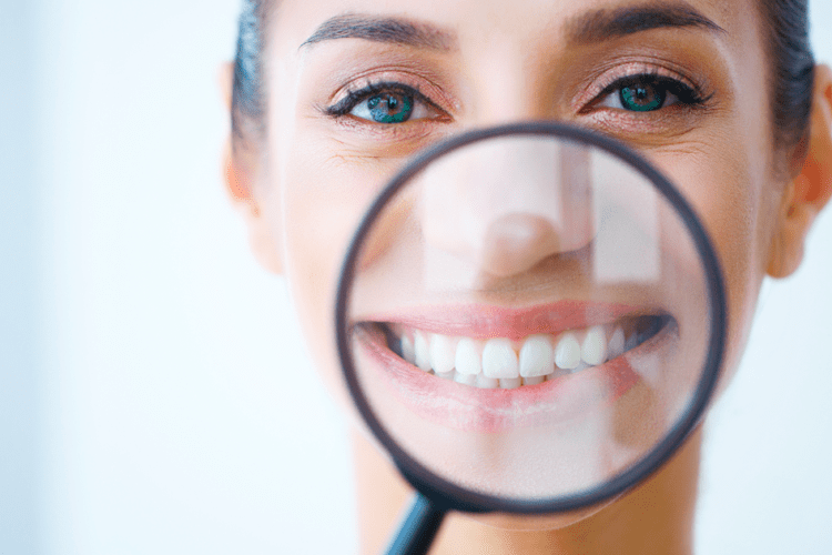 Mulher sorridente com lupa destacando o sorriso, representando a busca por um sorriso alinhado com aparelhos transparentes.