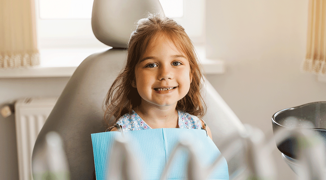 Menina sorrindo na cadeira do dentista, simbolizando a importância do acompanhamento profissional durante a troca dos dentes de leite.
