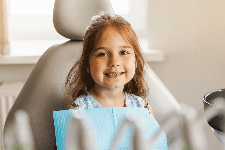 Menina sorrindo na cadeira do dentista, simbolizando a importância do acompanhamento profissional durante a troca dos dentes de leite.
