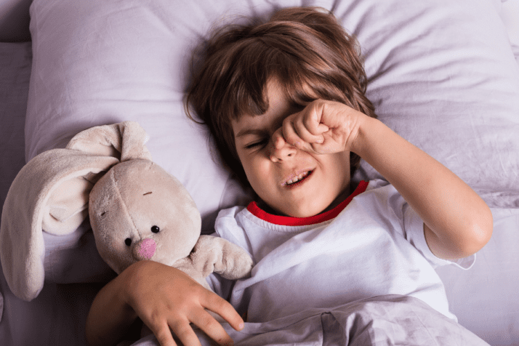 Criança esfregando os olhos na cama, demonstrando desconforto e sono perturbado causado pelo ronco.