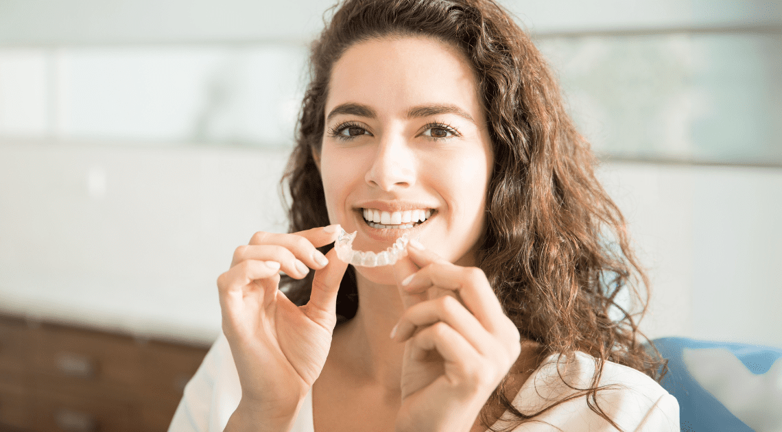 Mulher segurando um alinhador transparente, ideal para corrigir os dentes em qualquer idade.