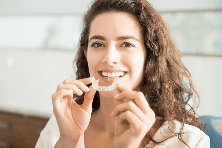 Mulher segurando um alinhador transparente, ideal para corrigir os dentes em qualquer idade.