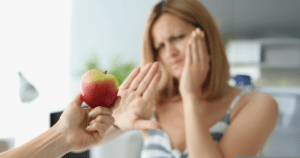 Mulher rejeitando uma maçã com expressão de dor, indicando dificuldades de mastigação causadas pela má oclusão dos dentes.