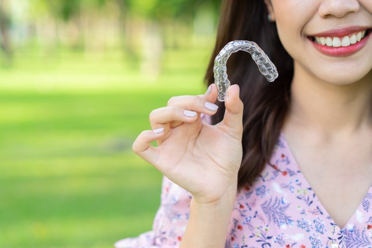 Mulher segurando aparelho transparente e sorrindo - Orthoclin