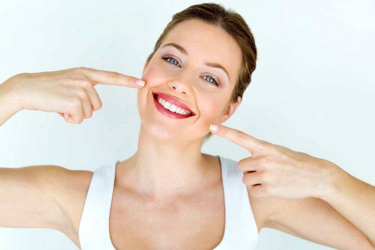Mulher sorrindo e apontando os seus indicadores para o seu sorriso