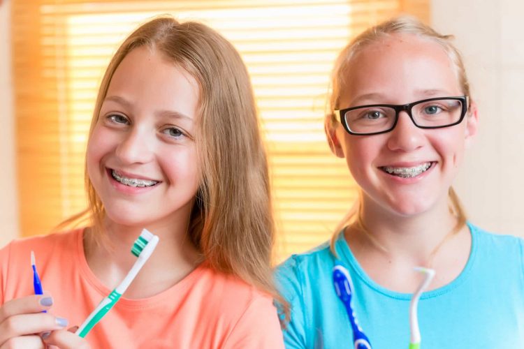 2 meninas sorrindo segurando escovas de dentes