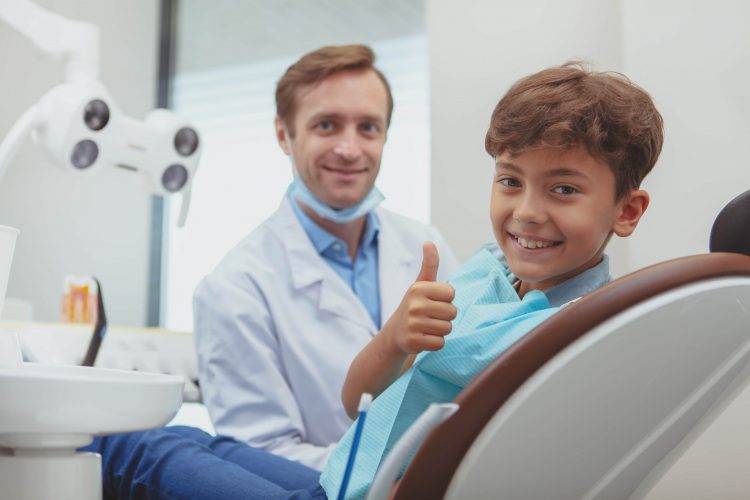 Jovem charmoso sorrindo, aparecendo os polegares após exame dentário na clínica