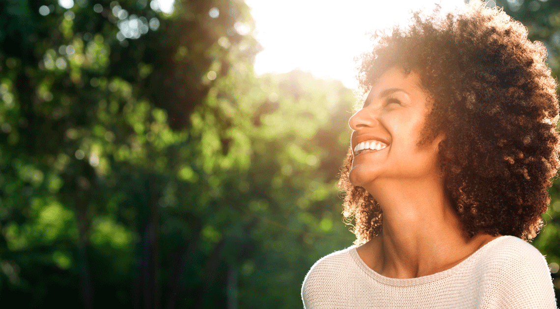 Mulher sorrindo ao ar livre após passar por tratamento ortodôntico estética, mostrando um sorriso saudável e perfeito.