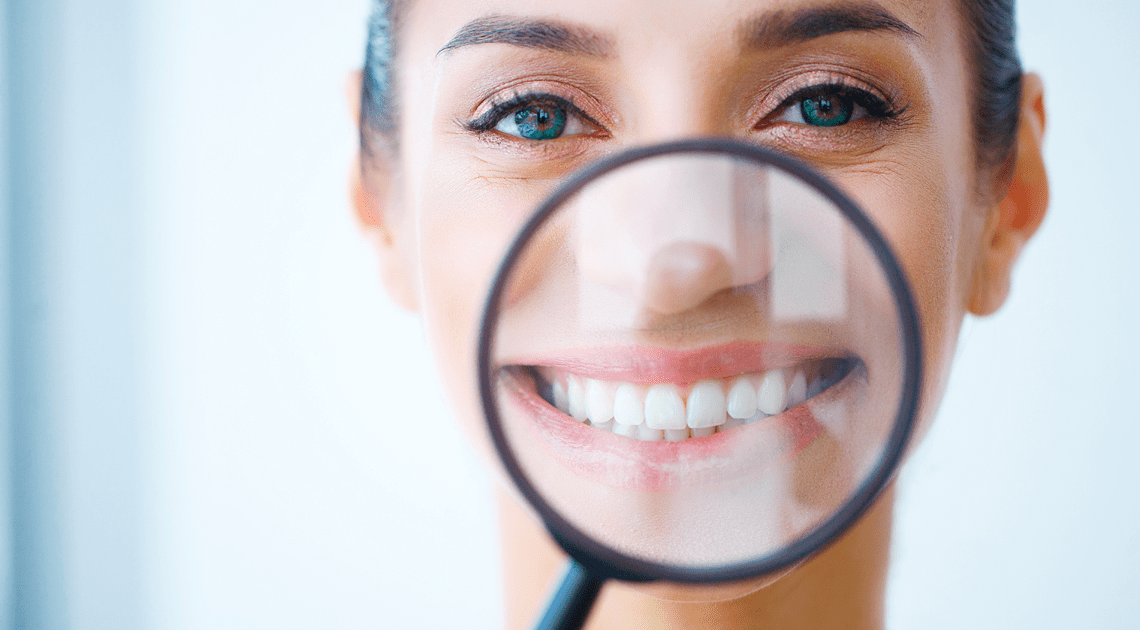 Mulher sorridente com lupa destacando o sorriso, representando a busca por um sorriso alinhado com aparelhos transparentes.